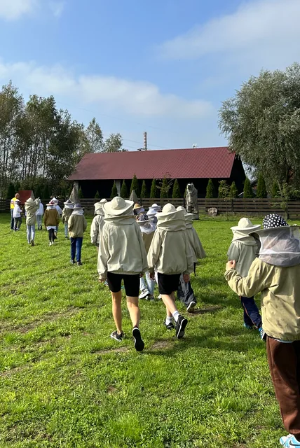 Grupowy spacer w kombinezonach pszczelarskich po terenie pasieki